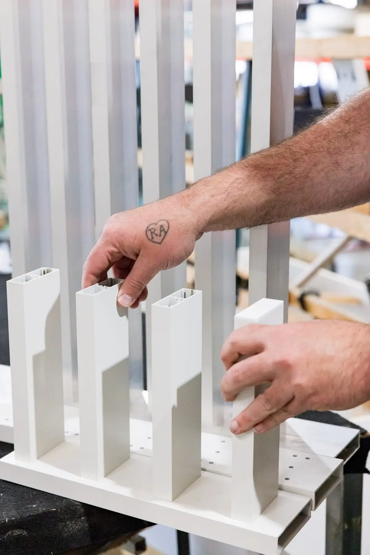 A fabricator's hands slotting white SlimLine battens into a machined baseplate on the workbench