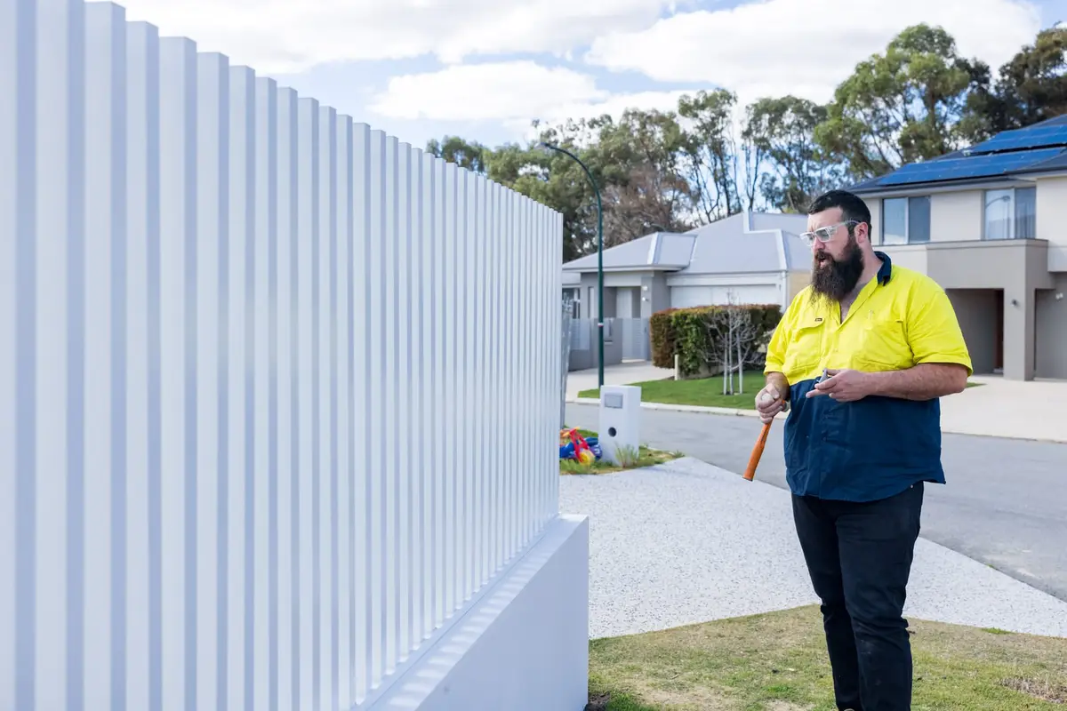 A fabricator in hi-vis working along a completed run of white SlimLine batten fencing